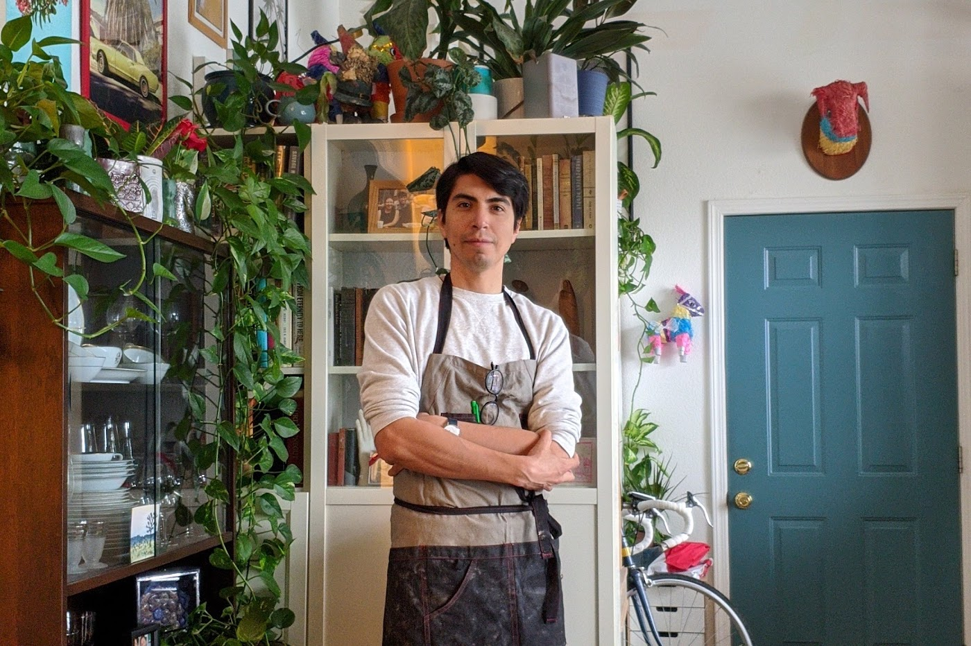Jose Aparicio wearing an artist's apron in his plant-filled home studio